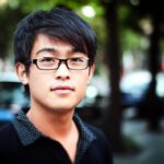 Young man standing on a street in Shanghai with a blurred background.
