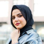 Elegant portrait of a stylish Muslim woman in a hijab sitting outdoors against an urban backdrop, showcasing modern fashion.